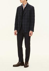 Marinblå rutiga blazer med slagkrage, i ulltyg, samsas med en svart tröja, skräddarsydda byxor och bruna läderskor.