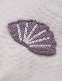 Broderi av en lila bladsilhouette med vit sömnad på en ljusbeige strukturerad tyg. Bladet har en vågig kant.