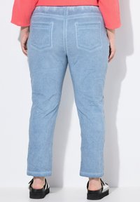 Pantalones de mezclilla azul claro con una textura arrugada, que cuentan con dos bolsillos traseros y un diseño recortado, combinados con sandalias de plataforma negras.