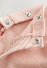 Primer plano de tela rosa con tres botones de presión plateados parcialmente abrochados en un borde acanalado.