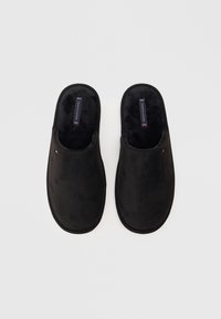 Zapatillas de ante negro con un suave forro interior, diseño de abertura trasera y mínima marca en la plantilla. Suela plana, sin patrones visibles.