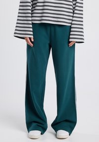 Person wearing teal wide-leg pants with side stripes, white sneakers, and a white long-sleeve shirt with black horizontal stripes.