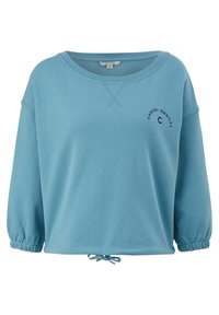 Sweatshirt bleu clair avec une coupe décontractée, col rond et manches longues. Présente des poignets froncés et un ourlet avec cordon de serrage. "IDENTITÉ DÉCONTRACTÉE" imprimé sur le devant.