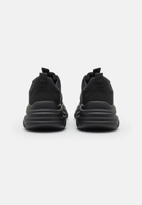 Chaussures de sport noires avec une tige en maille et un col rembourré, dotées d'une semelle épaisse amortissante et de languettes au talon pour un enfilage facile.