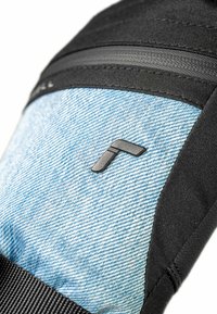 Denim-Rucksack mit schwarzen Nylonakzenten; verfügt über glatte Texturen, eine Reißverschlusstasche und ein Logo-Detail in Form eines stilisierten Buchstabens.