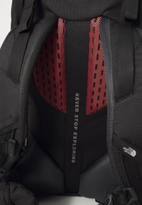 Svart ryggsekk med røde mesh-paneler, polstret støtte og hvit tekst som leser "NEVER STOP EXPLORING." Teksturert overflate og justerbare stropper.