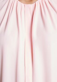 Gros plan d'un chemisier rose clair avec des plis froncés autour de l'encolure et un pli vertical central.