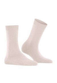 Un paio di calzini beige semplici, esposti in posizione verticale su uno sfondo bianco, che mostrano la texture e i polsini a coste.