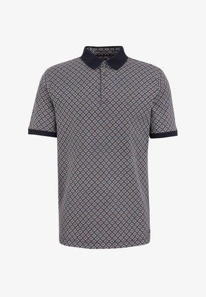 Kratkām piedurknēm polo krekls tumši zils ar atkārtojošu ģeometrisku rakstu sarkanā un krēmkrāsā. Tam ir tumši zila apkakle un apmalotās piedurknes. Mīksts audums.