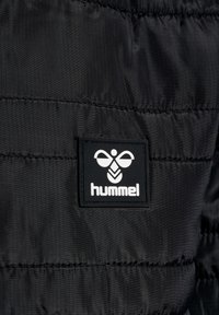 Svart vadderad jacka med quiltad yta. Har en Hummel-logotyp i vitt på en svart bakgrund, med subtil lyster i tyget.