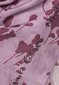 Sciarpa di un leggero viola con motivi floreali di un viola più scuro. Il testo "Manila Grace" è stampato in nero. Texture morbida e liscia con una leggera lucentezza.