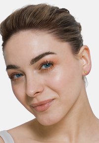 Boucles d'oreilles en or avec un design floral. Surface lisse avec de petites pierres précieuses. Cheveux tirés en arrière, mettant en valeur les boucles d'oreilles.