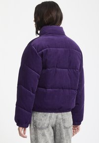 Paarse corduroy pufferjack met een hoge kraag, elastische manchetten en een gestructureerd, geborduurd ontwerp. Heeft een cropped pasvorm en eenvoudige lijnen.