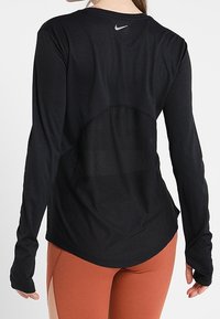 Schwarzes, langärmliges Sportoberteil mit einem Rückenpaneel aus Netzstoff und einem geschwungenen Saum. Verfügt über das Nike-Logo auf dem oberen Rücken, hergestellt aus leichtem Stoff.