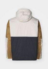 Polstret jakke med hætte, der har et farveskema i beige, brun og marineblå. Glat tekstur med et subtilt gittermønster.