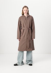 Brown, hooded, long-sleeve coat with a tie belt. The fabric appears smooth; model wears blue wide-leg jeans and black shoes.