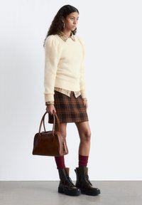 Cream puff-sleeve sweater, plaid shirt beneath, brown plaid skirt, burgundy socks, black combat boots, and brown handbag.