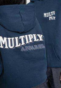 Navy blue hooded sweatshirt featuring bold white "MULTIPLY" and "APPAREL" text. Soft fabric, casual cut, and kangaroo pocket detail.