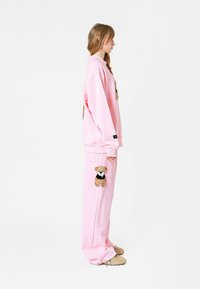 Conjunto de sudadera y pantalones de gran tamaño en color rosa, con un motivo de oso de peluche en el pecho y el bolsillo izquierdo del pantalón. Está hecho de una tela suave y cuenta con puños acanalados.