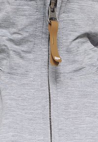 Gros plan d'une fermeture éclair en tissu gris fermée avec une tirette beige sur un vêtement.