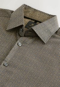 Camicia scura a fantasia con piccoli disegni floreali circolari beige, bottoni neri e colletto piegato, sdraiata su una superficie bianca.