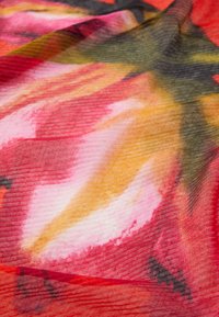 Tessuto colorato con un motivo floreale astratto nei toni del rosa, rosso, arancione e verde, caratterizzato da una superficie di tessuto texturizzata e una trama visibile.