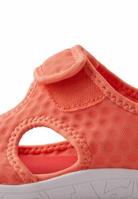 Coral fabric shoe with a Velcro strap, open sides, and white textured sole. Features stitching details and a circular cutout on the side.