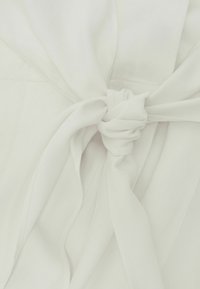 Nahaufnahme eines weißen Stoffs, der zu einem einfachen Knoten gebunden ist, mit glatter Textur und sichtbaren Nähten im Material.