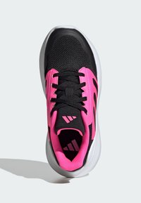 Chaussure de sport noire avec des accents roses, tige en maille et design à lacets. Elle possède une épaisse semelle blanche et des détails de logo au niveau du talon.