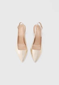 Ζευγάρι χρυσά γόβες με λουράκι στο πίσω μέρος, μυτερή μύτη, υφή και διάτρητες εσωτερικές σόλες σε ανοιχτό φόντο.