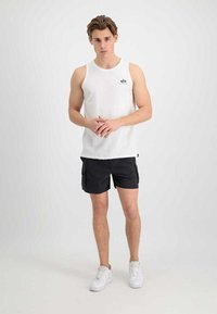 White tank top with a round neckline, paired with black cargo shorts featuring side pockets. Model wears white sneakers.