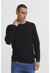 Black knit sweater with a round neckline, long sleeves, and ribbed cuffs. The fabric appears soft with a smooth texture.