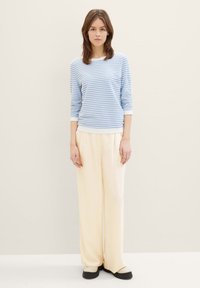 Chemise à rayures bleues et blanches à manches longues, coupe décontractée, avec un pantalon large couleur crème, associé à des chaussures crème. Textures simples et lisses.