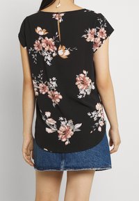 Blusa negra con flores en tonos rosa y blanco, mangas cortas, cuello redondo y detalle de abertura en la parte posterior. Combinada con una falda de mezclilla.