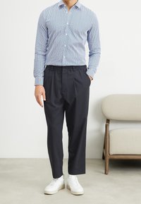 Camisa de botón azul claro con un pequeño patrón, combinada con pantalones negros de cintura elástica y zapatillas blancas. Diseño minimalista.