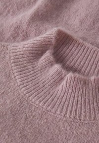 Gros plan d'un pull rose clair, mettant en avant une texture douce et un col côtelé. Le tissu paraît légèrement duveteux avec une finition lisse.