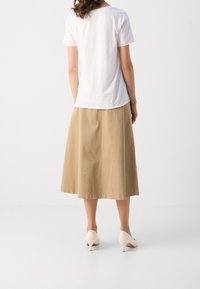 Bílý bavlněný tričko spárované s béžovou sukní ke kolenům; model v světlých lodičkách, viděný zezadu.