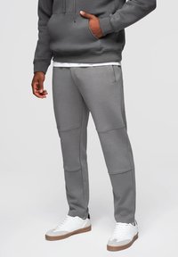 Szare dresy o tapered designie, wykonane z miękkiego materiału, z bocznymi kieszeniami i detalami szwów, zestawione z białymi trampkami.