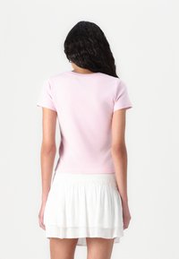 Short-sleeve pink top made of soft cotton, featuring a round neckline and a fitted cut, paired with a white tiered skirt.