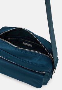 Borsa a tracolla in nylon color turchese con chiusura a zip, dotata di accessori in argento, finitura testurizzata e tasca frontale con zip.