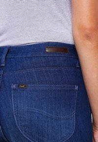 Vaqueros de mezclilla azul oscuro con una etiqueta de cuero de Lee, que cuentan con bolsillos traseros con detalles de costura y una textura suave. Tejido a rayas por encima de la cintura.