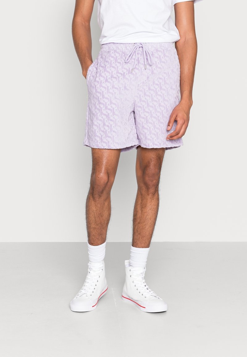 Shorts de bain lilas clair avec un motif de vagues texturé, taille élastique, fermeture à cordon, et poches latérales, associés à des baskets blanches.