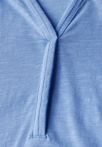 Tessuto blu chiaro con una texture liscia. Presenta un design a V e una cucitura centrale. Il materiale appare morbido e informale.
