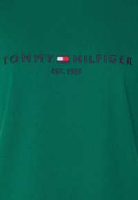 Zelené bavlněné tričko s vyšitým logem "TOMMY HILFIGER" v námořnické modři, s malým červeným a modrým obdélníkovým detailem a nápisem "EST. 1985."