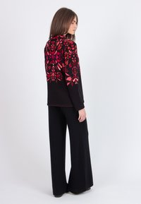 Black sweater with intricate red and pink floral patterns on the back, paired with black wide-legged pants. The fabric appears soft and textured.