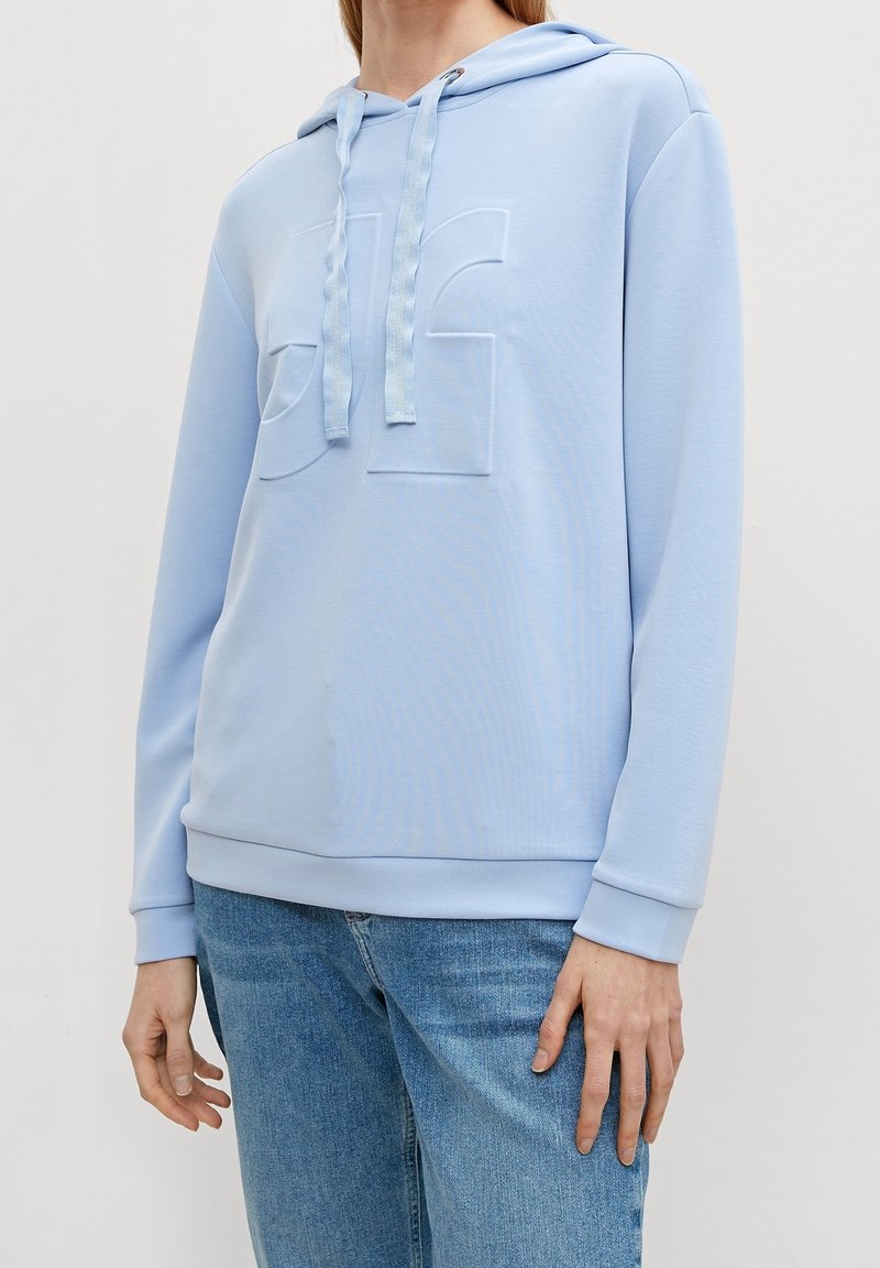 Felpa leggera blu chiaro realizzata in tessuto morbido, con logo in rilievo sulla parte anteriore, cappuccio con cordoncino e polsini e orlo a costine. Abbinata a jeans in denim.