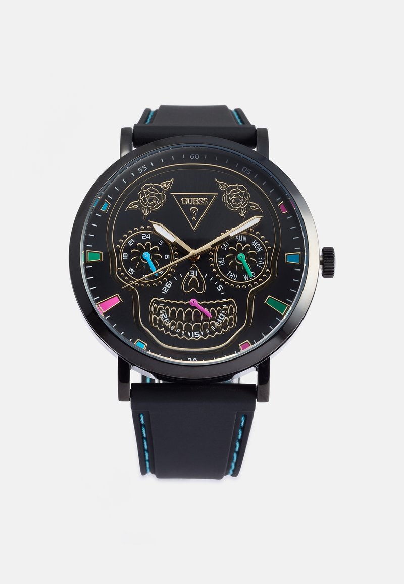 Montre-bracelet noire avec un cadran tête de mort, des yeux floraux, des marqueurs d'heure colorés et trois sous-cadrans pour les fonctions 24 heures, jour et date.