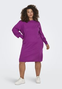 Lila stickad klänning med långa ballongsärmar, ribbade manschetter och avslappnad passform, i kombination med vita sportskor.