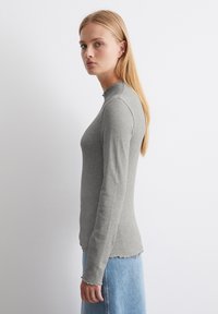 Grijze geribbelde langemouwen top met gegolfde halslijn en zoom; gecombineerd met een lichtblauwe denimrok. Glad textuur, strakke pasvorm.