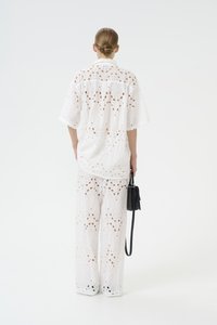 Completo in cotone bianco composto da una camicia e pantaloni a gamba larga con intricati intagli e motivi floreali. Completato con una borsa nera.